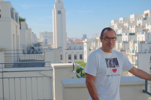 Luc Royet sur la terrasse de son appartement avec la mairie de Villeurbanne en arrière-plan. © Bertrand Enjalbal