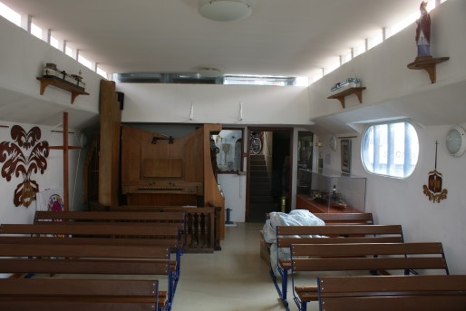 L'intérieur de la chapelle, dans l'ancienne partie transport de la péniche. Au fond à gauche, un orgue pour l'office. Au mur, un chemin de croix illustré en bois ouvragé. Au fond à droite, la maquette d'un ancien bateau remorqueur dans sa vitrine. ©MP/Rue89Lyon