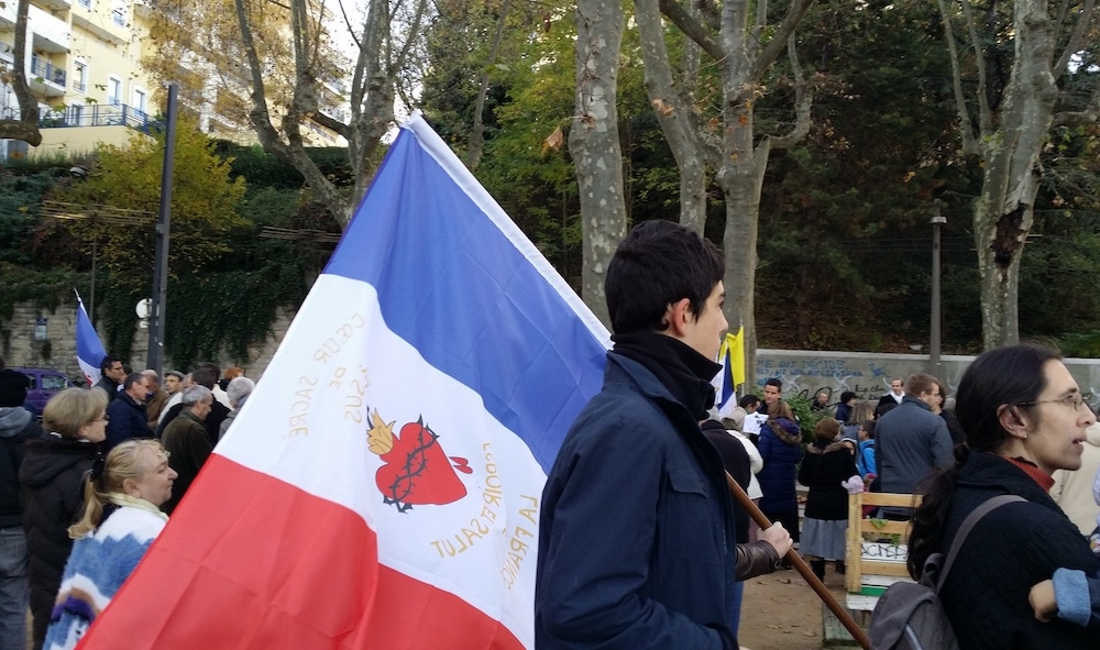 Le rassemblement des cathos tradis pour "sauver" l'église Saint-Bernard. Des drapeaux français ornés du "cœur sacré de Jésus" ont été distribués aux participants. ©LB/Rue89Lyon
