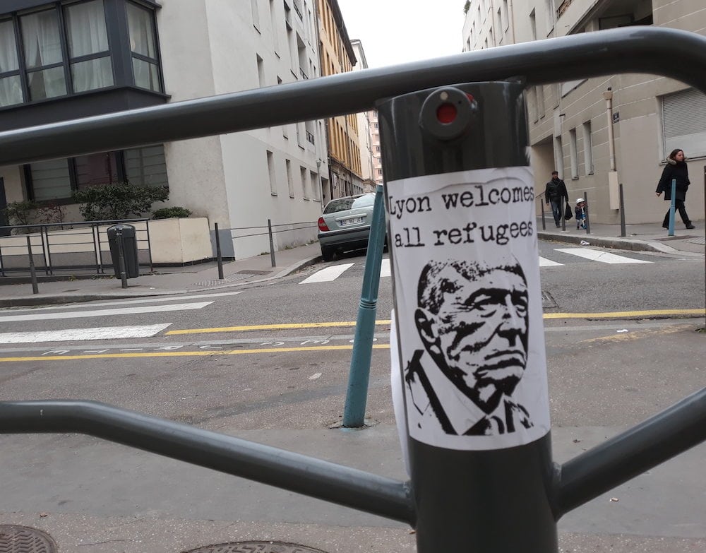 "Lyon welcomes all refugees". Affiche avec le visage de Gérard Collomb photographiée en novembre 2018 devant l'école Gilbert Dru, à la Guillotière (Lyon 7e). ©LB/Rue89Lyon