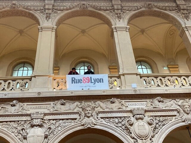 Deux journalistes de Rue89Lyon derrière la banderole du site d'info, au Palais de la Bourse à Lyon. ©DD/Rue89Lyon